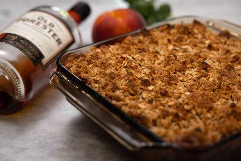 Bourbon Peach Crisp in baking dish next to a bottle of Old Forester 100 proof