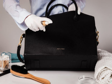 Spraying a leather purse with a cleaning spray