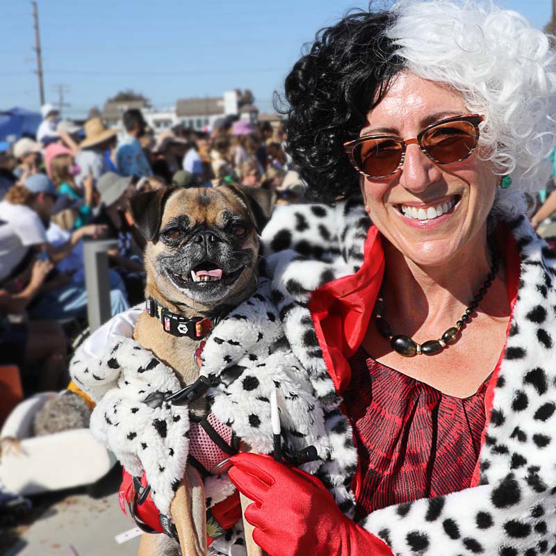 2022 Haute Dog Howl'oween Parade with Cruella de Vil Holding her Pug who is wearing a 101 Dalmatian Winter Coat Dog Costume - Photo credit JustinRudd.com/howloween.