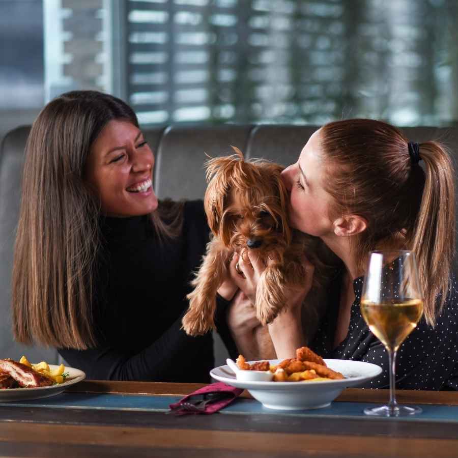 Two young women smiling and loving their puppy at a pet-friendly restaurant, celebrating National Best Friends Day!