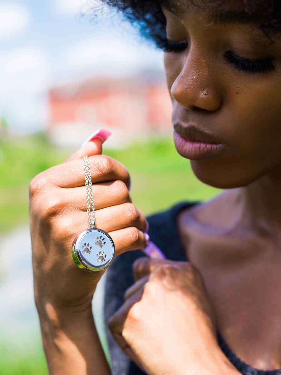 Black woman holding up the lovely Paw Print Memorial Locket where you can safely insert the ashes of your beloved pet and you customize the background color of the locket to be used as an aromatherapy essential oil diffuser.