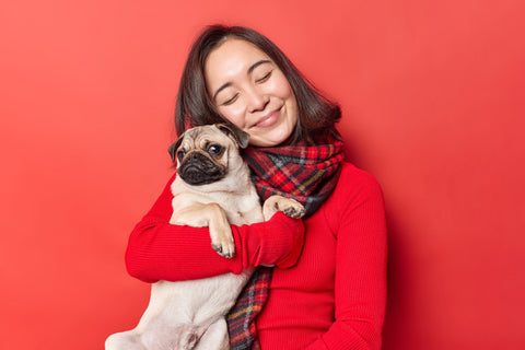 happy-young-asian-woman-embraces-pug-dog-with-love-expresses-love-favorite-pet-have-friendly-relationships-enjoys-company-best-friend-wears-jumper-with-scarf-isolated-red-background