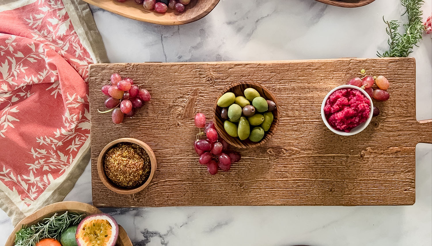 Wooden charcuterie board with olives, dips, and grapes