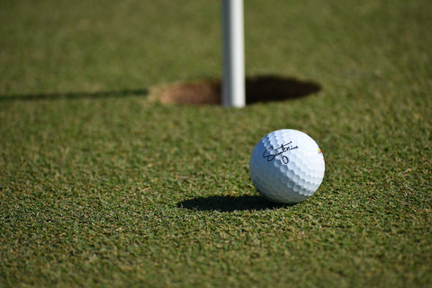 Image of a Saintnine golf ball next to the hole. 