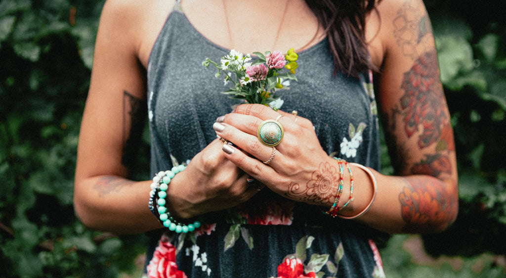 femme portant des bracelets et bijoux en pierres fines et portant un petit bouquet de fleurs entre ses mains