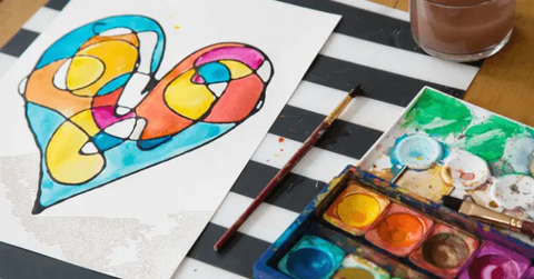 a watercolor painting of a multicolored heart with a set of watercolors next to it