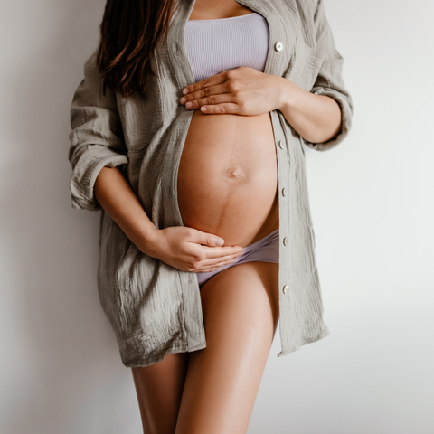 bottom half of woman in linen shirt holding baby or post partum bump on tummy