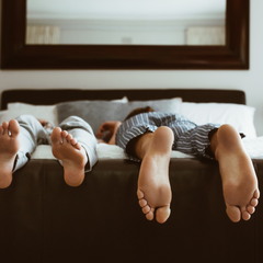 bare feet hanging off the end of a dark wooden bed in striped pyjamas