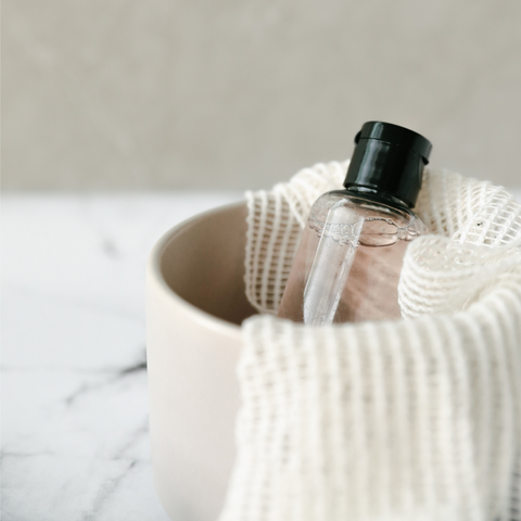 beauty product in clear bottle inside soft pink basket with white fabric