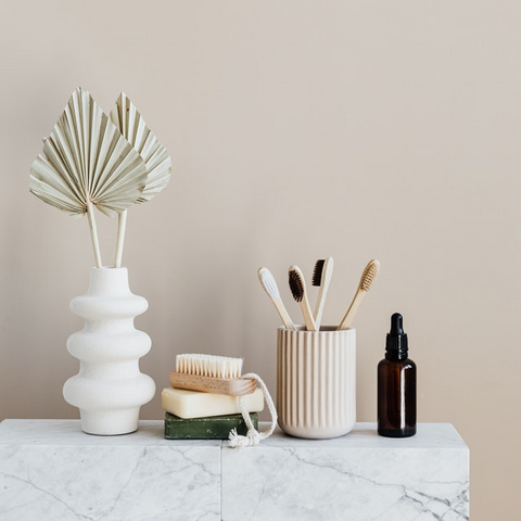 range of beauty products on a marble shelf including soap, bamboo toothbrush and oil bottle
