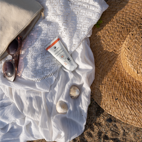 organic sunscreen on sandy beach with sunhat, sunglasses and coverup