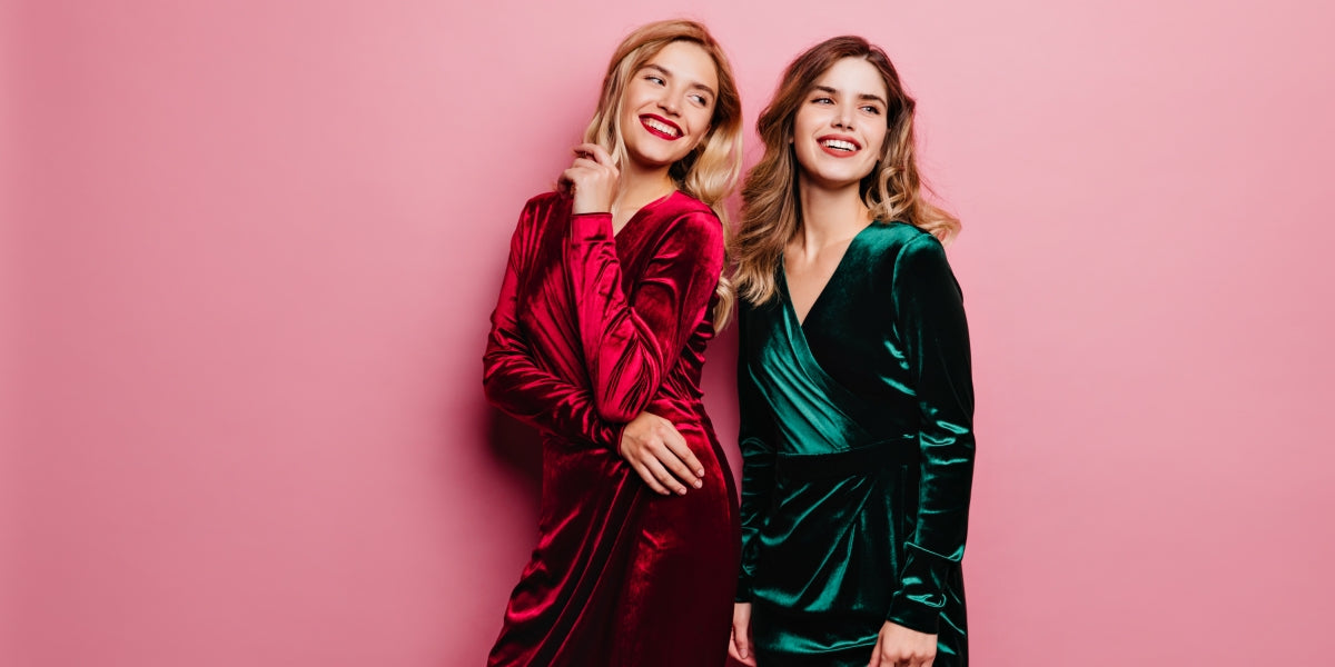 Dreamy ladies in stylish velvet dresses posing with cute smile. Indoor photo of attractive white girls isolated on rosy background.