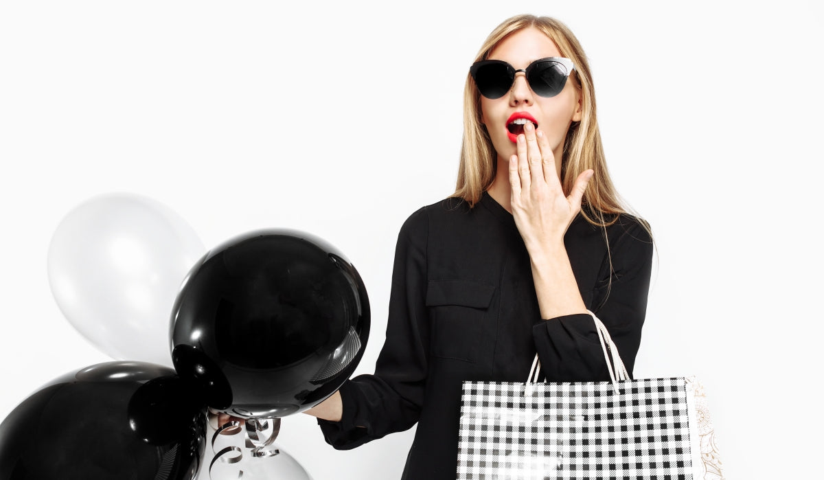 Elegant shocked girl in black dress with sunglasses, handbag and black ball in her hands isolated on white background. black friday, shopping, discounts