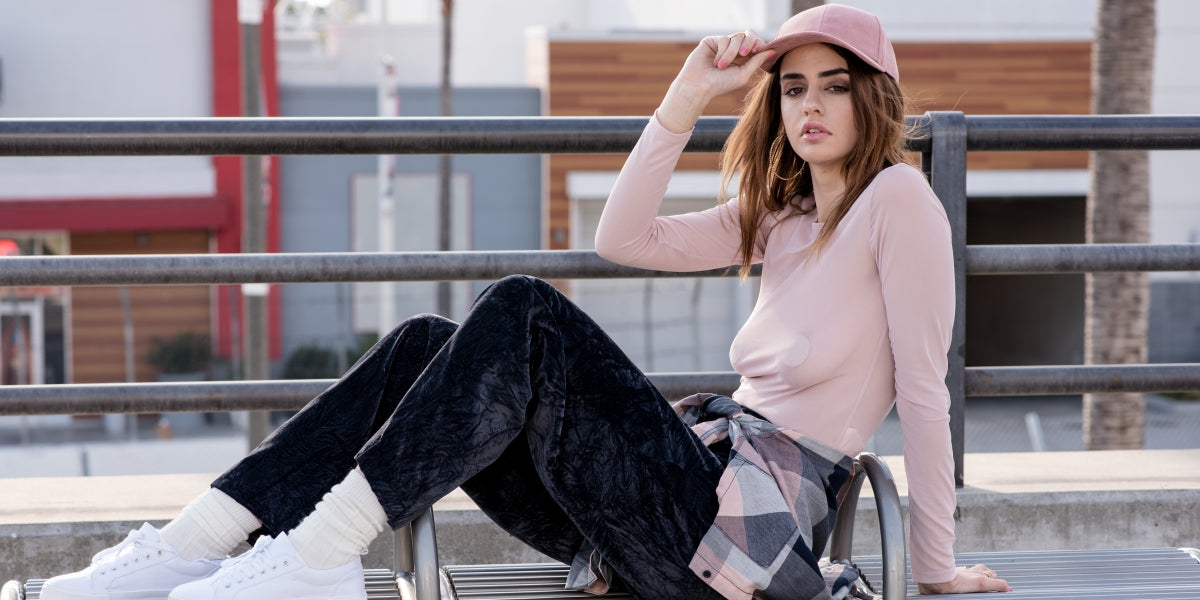 Street style fashion. Pink sheer long sleeve blouse with a pastel multi-colored pastel flannel, black crushed velvet pants, coordinating with a pink hat.