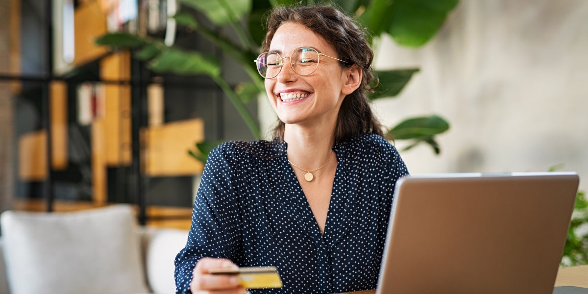 Young happy woman doing shopping online with laptop. Portrait of excited woman holding credit card and buy on an e-commerce site. Beautiful laughing girl paying online bills using debit card.