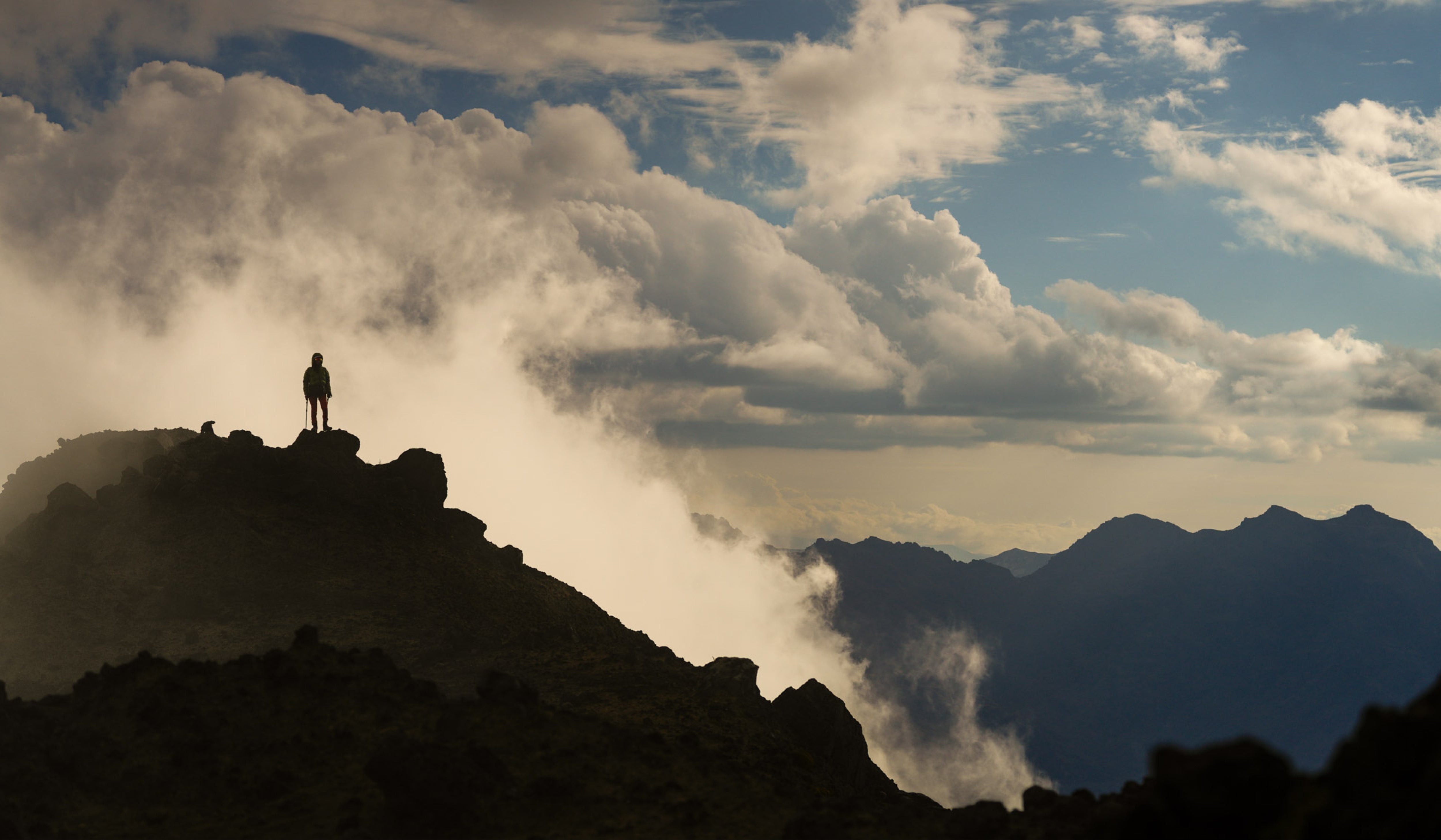 Photo courtesy of Andrés Molestina, depicting person standing at the summit of a landscape during sunset.