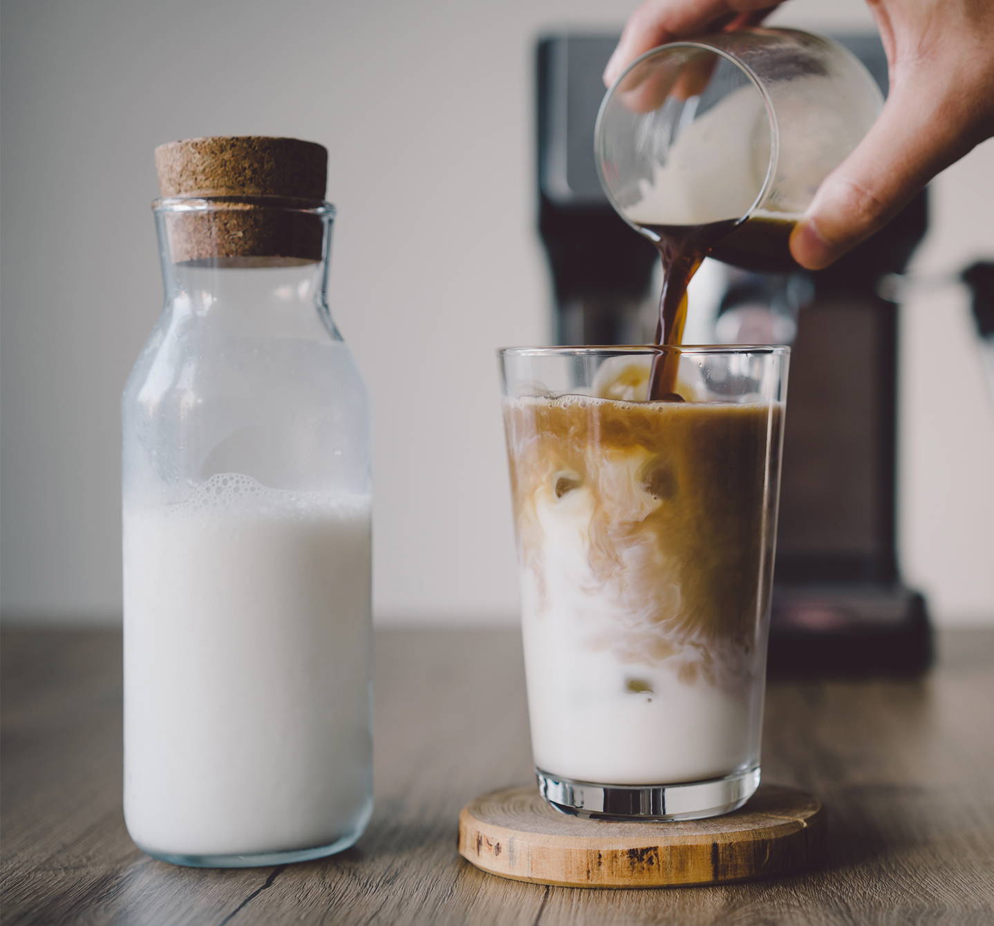 Coffee is being poured into a glass of milk with ice cubes