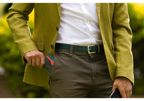 Man in a lime green blazer and brown trousers pulls out his leather card holder from his pocket