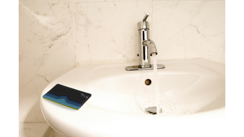 a blue leather wallet sits on the edge of a sink getting splashed with water