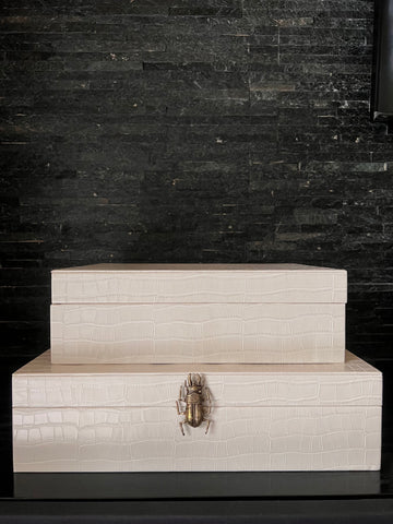 Dos cajas blancas de piel sintética con un escarabajo de latón como asa, un accesorio de decoración para el hogar