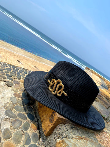 Sombrero negro de verano con una hebilla de serpiente dorada en una playa