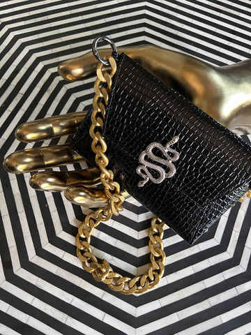 Bolso de mano de piel sintética negra con una pesada cadena de oro sobre una mesa de rayas blancas y negras