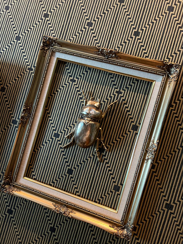 Un marco dorado sobre papel tapiz de rayas con un escarabajo de bronce