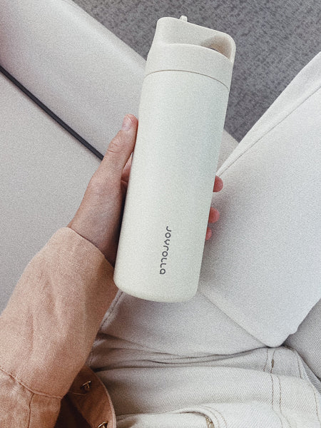 a hand holding a beige reusable drink bottle with the joyrolla logo.
