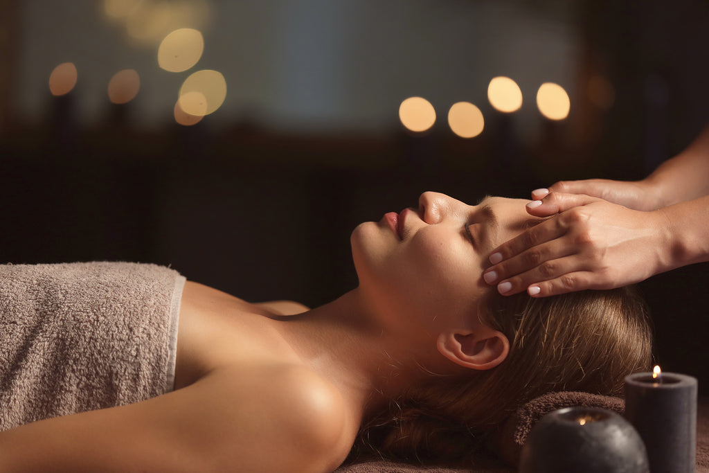 A person receiving a relaxing facial massage in a tranquil setting with soft lighting and candles in the background