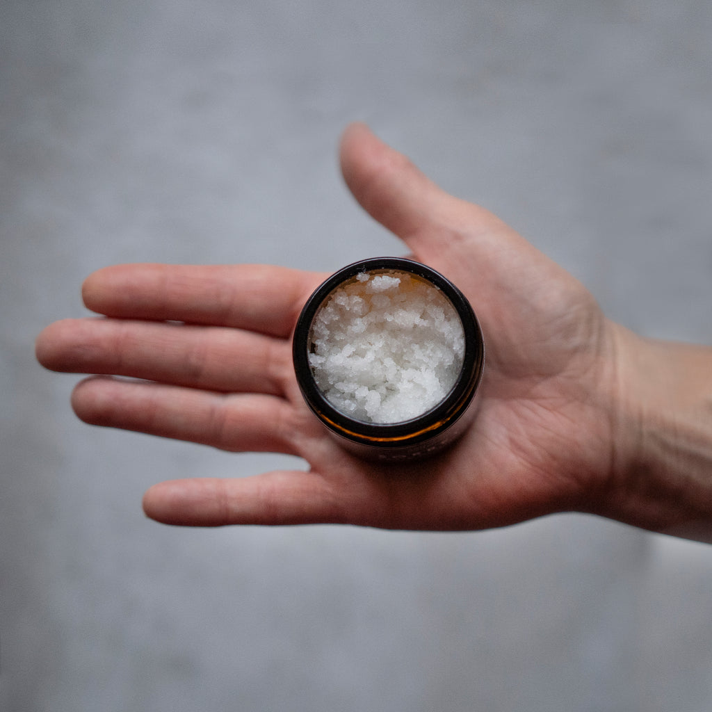 open flat hand holding amber jar no lid of white facial sugar scrub