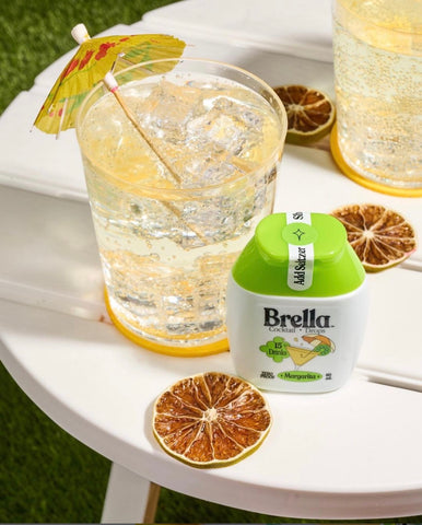 Lifestyle image of Margarita by Brella Drops. Dried orange slices, product and cocktail sitting on the edge of a table.