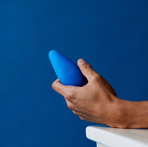 Image of a hand holding the Personal Massager by Butter Wellness, against a blue backdrop