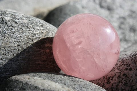 Example of a Rose Quartz Sphere Among Gray Rive Stones - Crystals for Abundance