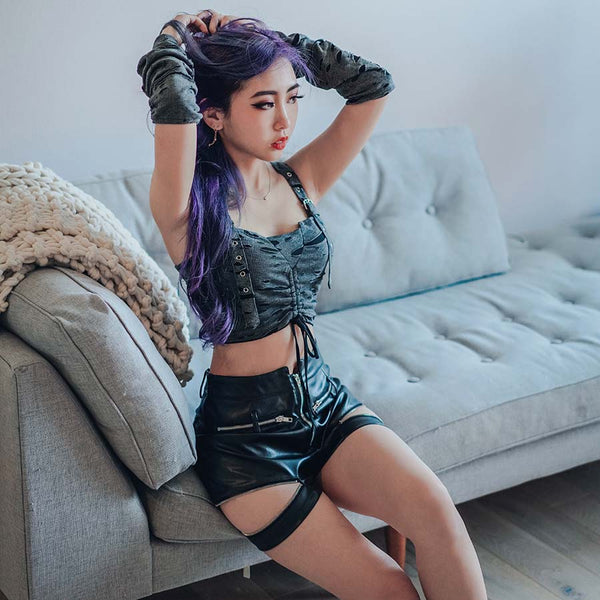 purple hair model wearing a rave outfit with strappy top and pleather shorts