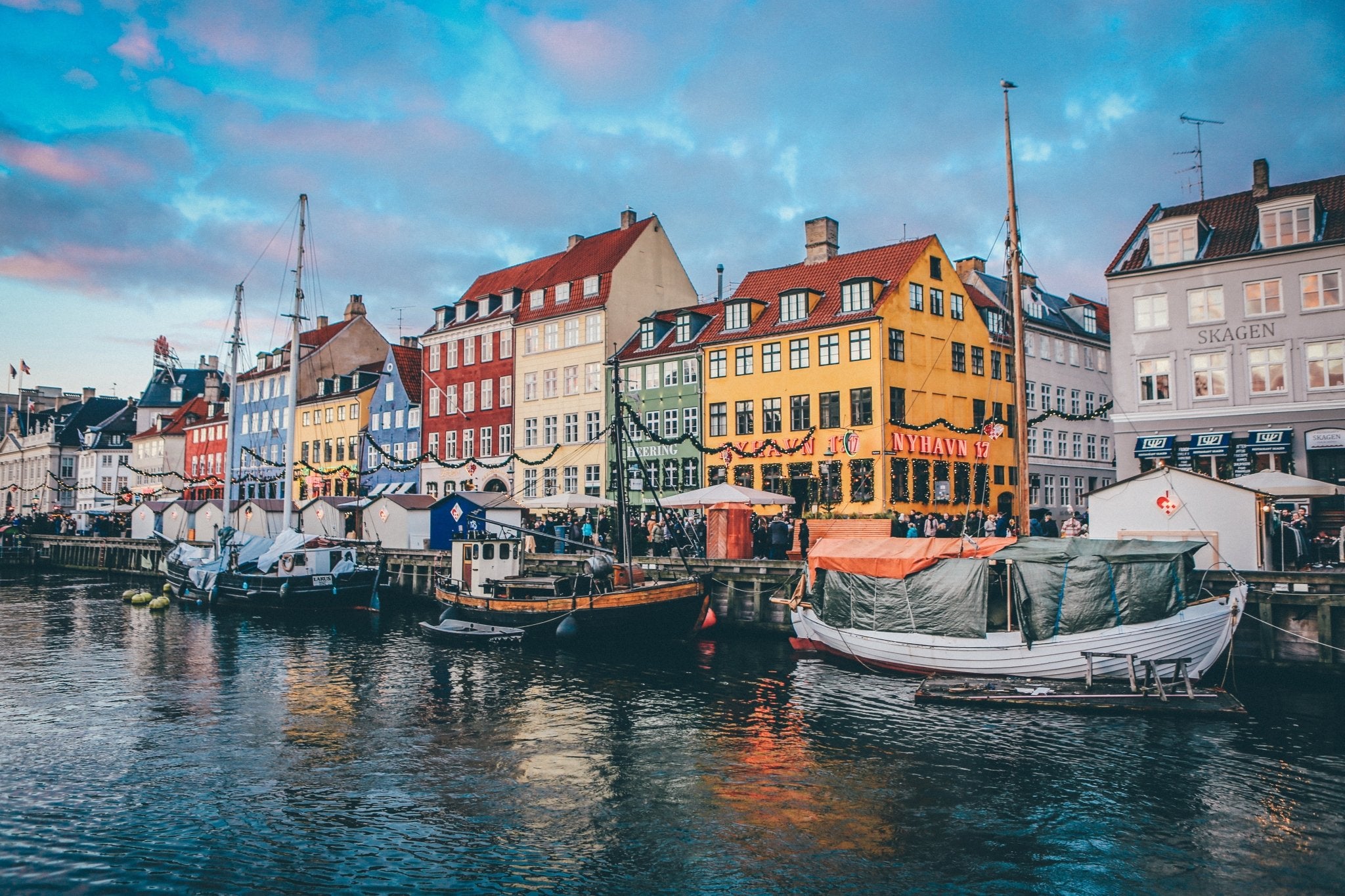 Multiple boats tied to the shore in front of colorful buildings in Copenhagen, Denmark