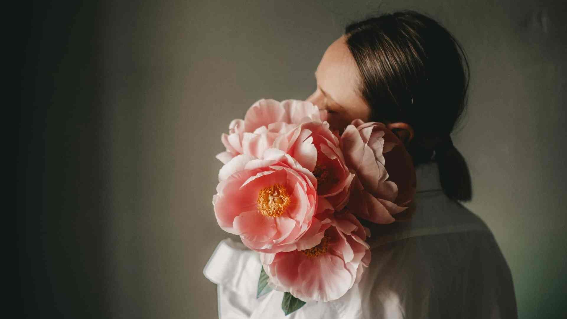 A woman has her back to the camera, holding a large pink flower to her face that covers her profile picture.
