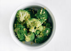 white bowl of sesame broccoli with lemon zest on top