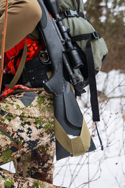 Closeup of the butt of a gun in a rifle sling while a hunter hikes in winter