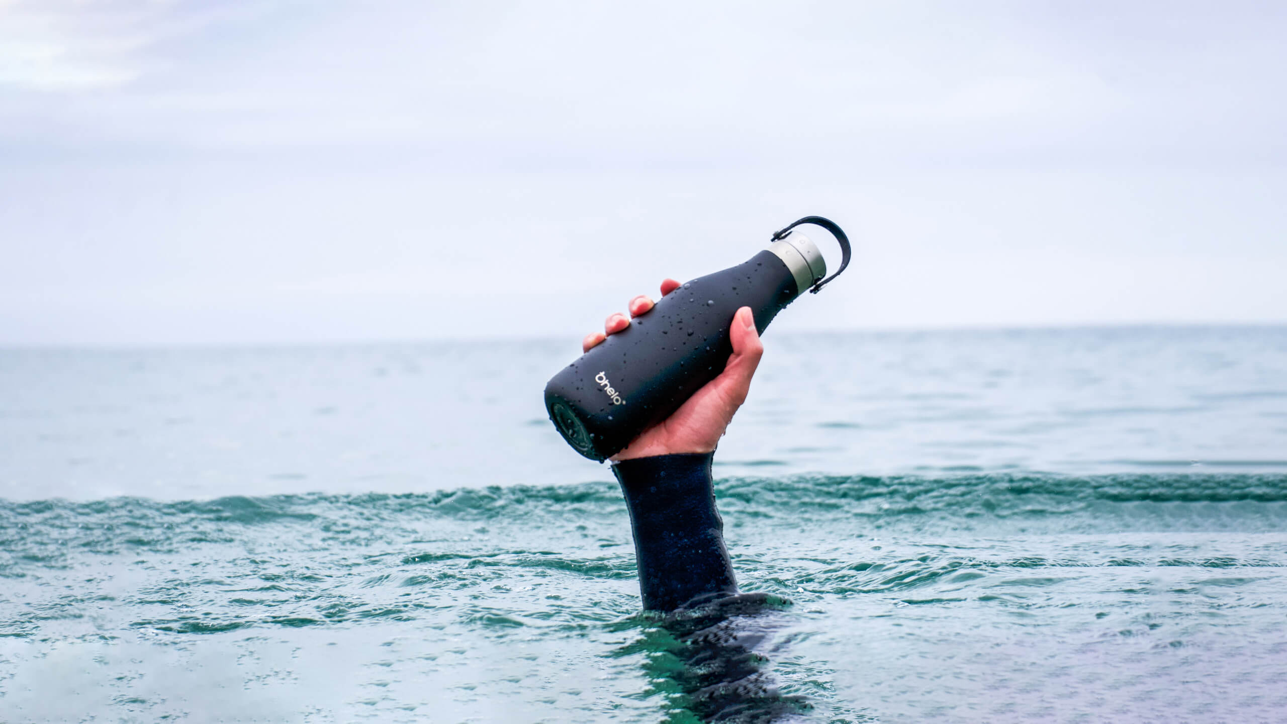 Ohelo black insulated water bottle being held by hand coming out of the sea