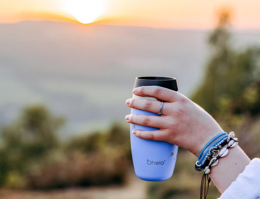 Ohelo leakproof travel mug in blue swallows design, held in hand with sunset view