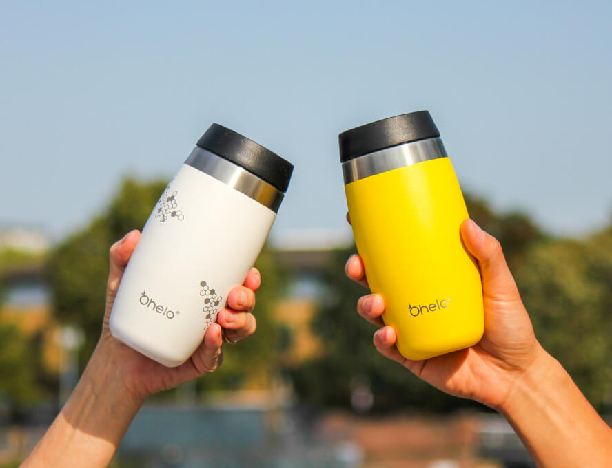 White and yellow reusable coffee cup in "cheers" pose