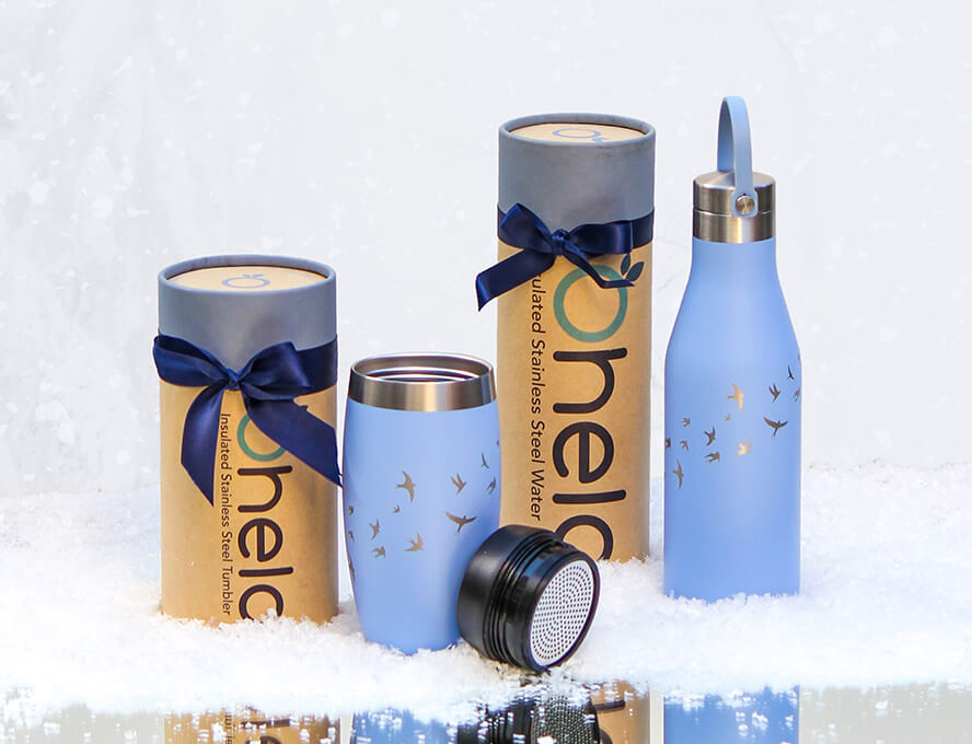 Ohelo blue swallows bottle and travel mug sitting in a snowy setting with blue christmas ribbons around their sustainable packaging as gifts