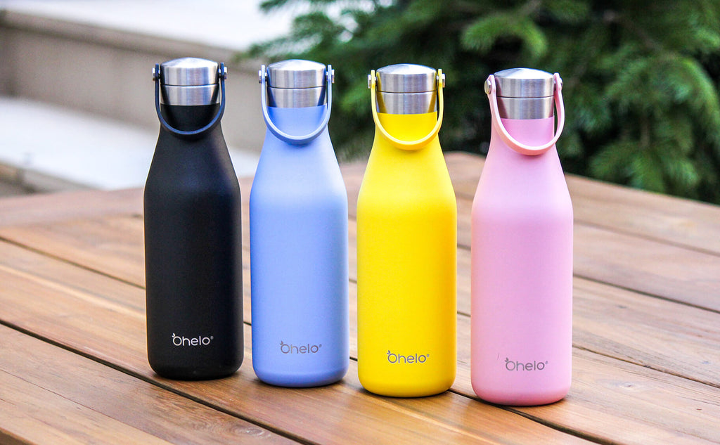 Ohelo plain bottles in black, blue, yellow and pink lined up on a wooden table