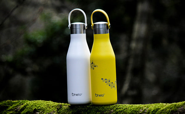 Ohelo vacuum insulated stainless steel water bottles in plain white and yellow bee designs in a forest setting