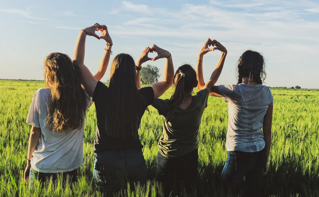 Women in field making heart shapes with their hands