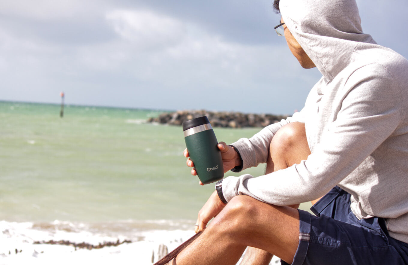 Man on beach holding Ohelo green reusable coffee cup