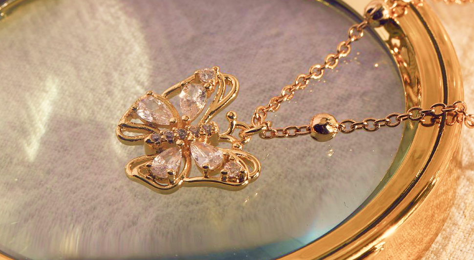 A golden necklace with a butterfly pendant that is embedded with beautiful gemstones