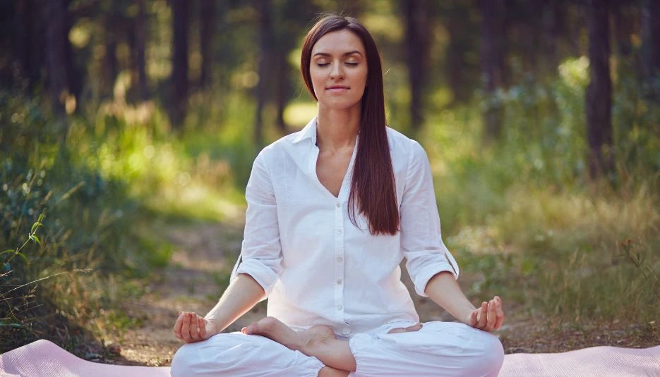 a woman meditating on a mat in the middle of a forest