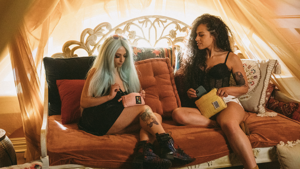 Two girls sitting on burnt orange couch preparing to smoke.