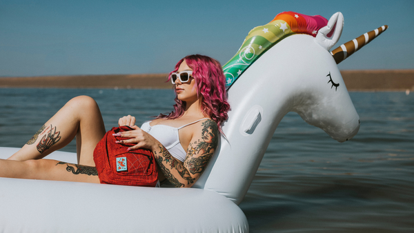 Woman sitting on unicorn float at lake with red Hot Box mini backpack